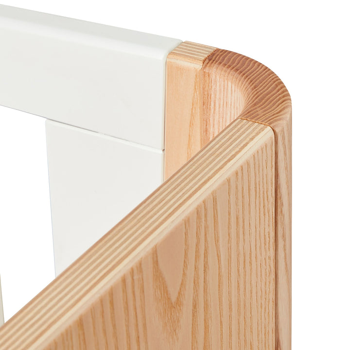 This image is a close up of the top right hand corner of the Hera Cot Bed, showing off the real wood grain and stunning wood finish.